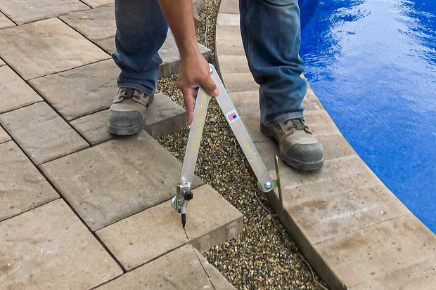 Person using a tool on a stone patio next to a pool